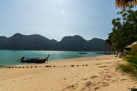 A beautiful Phi Phi Island beach Thailand landscape featuring a traditional boat set against majestic mountainsの写真素材