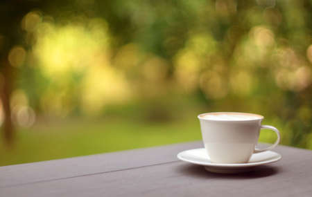 Soft focus on white cup of coffee on light gray wood table with blurred green leaves in a background, relax nature environment coffeehouse, lifestyle concept with copy space for your textの写真素材
