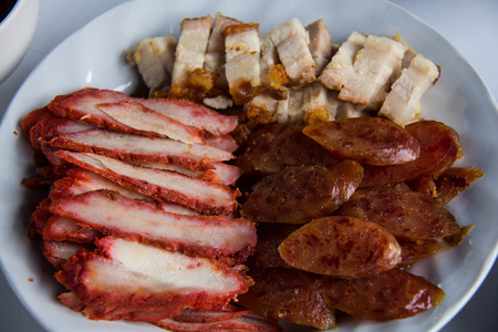 Crispy roasted belly pork, roasted red pork and chinese sausage on white dishの写真素材