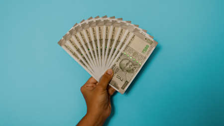 Man holding multiple five hundred rupee notes in hand, blue backgroundの写真素材