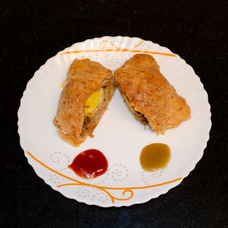 Indian egg puffs cut into two pieces served with chilli and tomato sauce in a white ceramic trayの写真素材