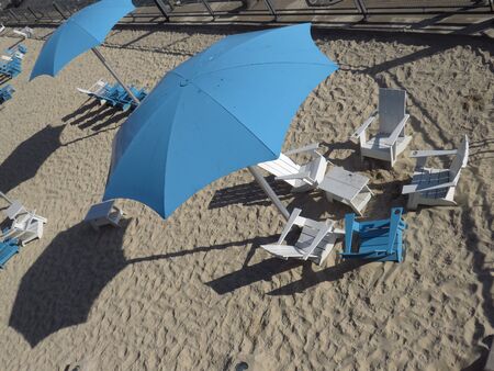 View from above of a blue beach umbrella and set of wooden table and chairs in blue and white. White and smooth sand Montreal beach. Canadaの写真素材