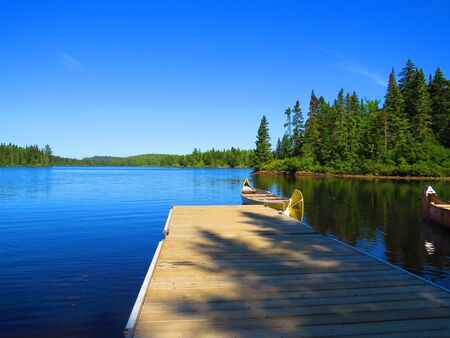 Canadian rabaska canoe resting by the calm water in beautiful Wapizagonke lake. Mauricie National Park, Quebec Canada.Look out point with blue sky and tranquil waters landscapeの写真素材