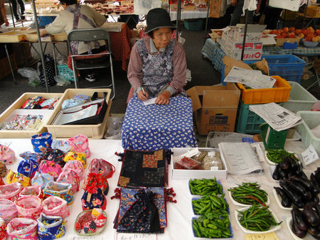 Takayama, Japan; September, 18, 2010: Japanese woman sitting at her local market stall. Sell handmade Japanese cloth products and vegetablesのeditorial素材