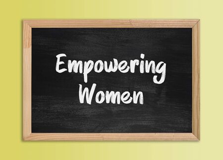 Vintage chalkboard in wooden frame on yellow background. Chalkboard isolated with "Empowering Women" message.の写真素材