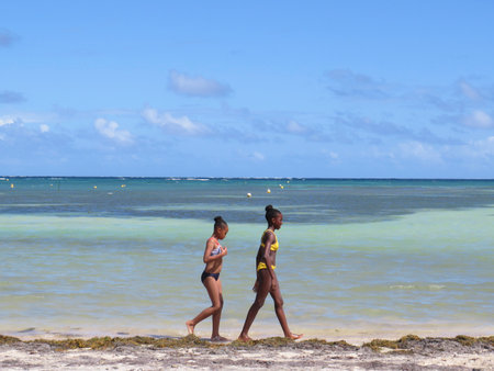Martinique, French West Indies; December 10, 2019: Two Antillean girls walk on beach of Martinique Island, Caribbean Sea with turquoise waterのeditorial素材