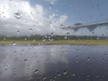 Close-up of water drops on glass and unfocused background of airplane wing entering runway.の写真素材