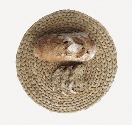 Top view texture of delicious baked and cut fresh bread on handmade round beige wicker tablecloth isolated on white background. Freshly bread slices.の写真素材