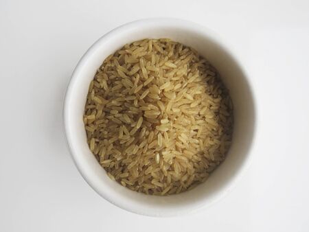 Organic raw Brown Rice in a white bowl on white background, top view. Integral Wholegrain.