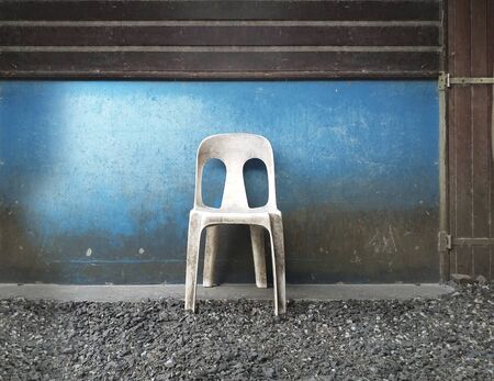 Old plastic white chair on wooden wall and blue background. Gravel floor. Tropical culture.の写真素材