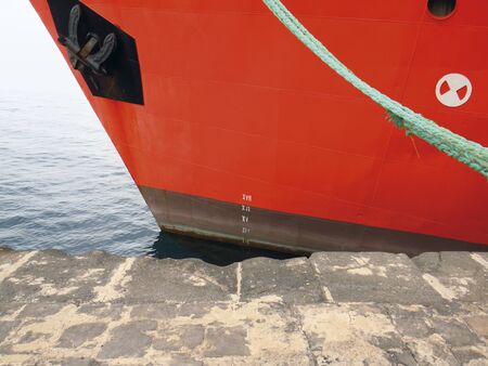Prow front view of a large red merchant ship moored at the port quay. Rope tied to the hull of a bulk carrier ship moored in a harbor.の写真素材