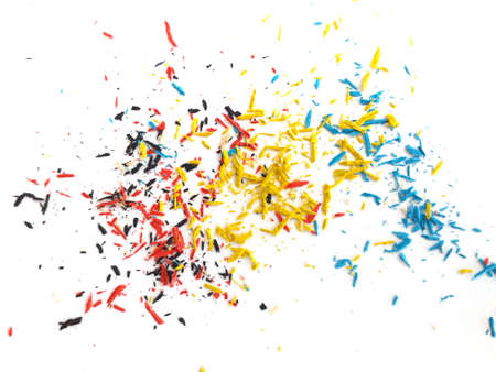 Small shavings of yellow, blue, red and black crayons on white background. Crayon shavings Artistic...
