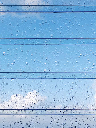 Abstract texture of drops of rain on a window glass. Clean background view of water drops on glass over a blue sky. Rain water drops on glass with tropical blue sky background with clouds.の写真素材