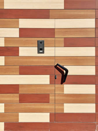 Background of a street door made of wooden slats of different colors, a black doorknob and a modern...
