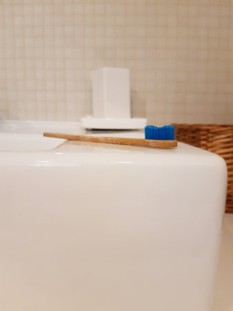 Perspective view of bamboo toothbrush and empty ceramic toothbrush holder on white sink and other...