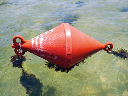 Close up of chained red conical buoy floating in turquoise waters of lagoon in caribbean sea....