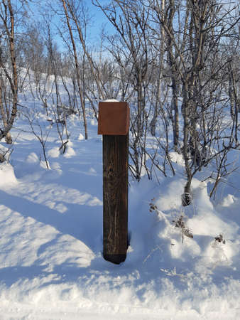 Wooden post in Snowy lapland landscape. Hiking trail signage with snow on the polar circle under blue sky. Nature of the Nordic countries.の写真素材