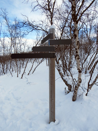 Trail marking post in snowy landscape on the polar circle. Solid wooden post with arrows indicating paths in the middle of the snow.の写真素材