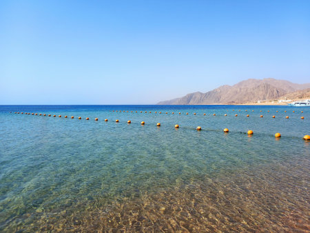 Line of yellow buoys floating in the water of the Red Sea. Panoramic view of Dahab coastline in the Egyptian desert. Beaconing and aquatic signage.の素材