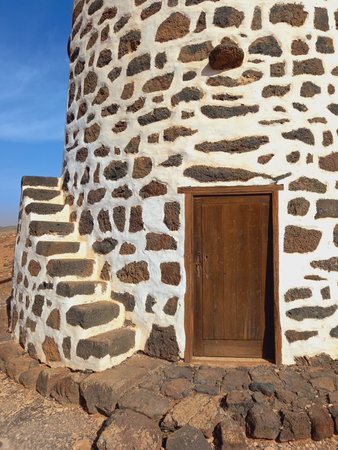 Front entrance of Traditional Fuerteventura windmill under blue sky. Circular windmill with blades...