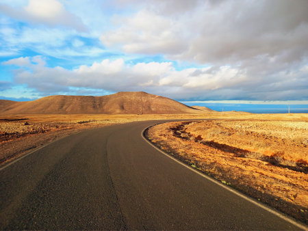 Panoramic view of long empty desert asphalt road crossing El Corralejo Dunes Natural Park in Fuerteventura. Canary Islands. Lonely road in a desert area and blue sky. Driving and Landscape concept.の写真素材