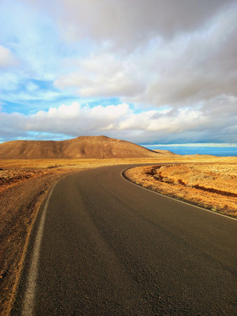 Panoramic view of long empty desert asphalt road crossing El Corralejo Dunes Natural Park in Fuerteventura. Canary Islands. Lonely road in a desert area and blue sky. Driving and Landscape concept.の写真素材