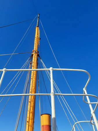 Mast of a ship from below. Big mast, railing and ropes of merchant ship under blue sky. Nautical and...