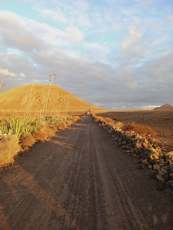 Volcanic landscape. Dirt road in Desert area with stones, rocks and sandstone and silhouette of volcano slopes on the horizon. Landscapes and nature.の写真素材