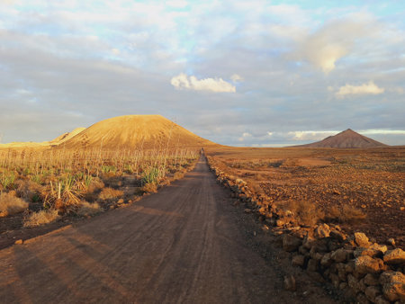 Volcanic landscape. Dirt road in Desert area with stones, rocks and sandstone and silhouette of volcano slopes on the horizon. Landscapes and extreme nature.の写真素材
