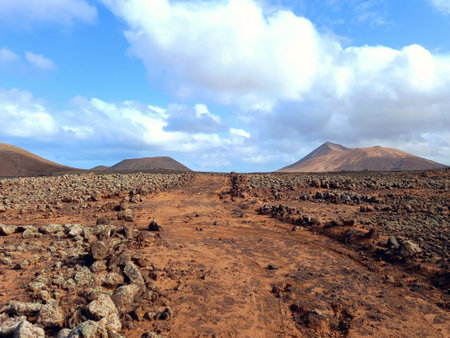 Volcanic landscape. Dirt road in desert landscape under blue sky and silhouette of volcano slopes on the horizon. Nature and extreme sports.の写真素材