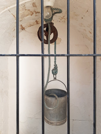 Tin bucket in a decorative fountain. Close-up of a well pulley, bucket, and rope. Front view of a zinc bucket in an old medieval village well.の写真素材