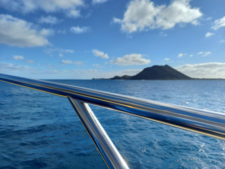 Panoramic view of the sea and volcanic island from the deck of a ship. Ship's railing as it sails under a blue sky with volcanic land on the horizon. Seascape.の写真素材