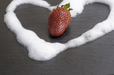Strawberry in the middle of a circle of cream on slate.の写真素材