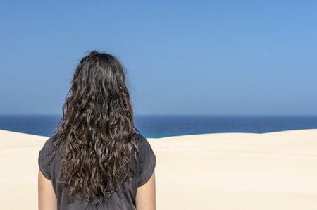 Rear View of brunette woman looking at sea from a white dune in Fuerteventura, Spain.の写真素材