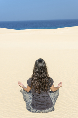 Rear View of brunette woman doing yoga in a dune in Fuerteventura.の写真素材