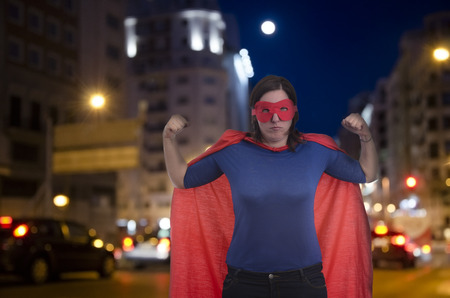 Woman superhero with red cape in strong position in a night street.の写真素材