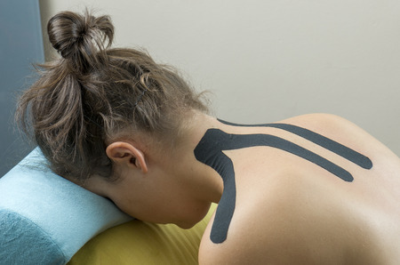 Physiotherapist putting on black kinesio tape on woman patients back.の写真素材