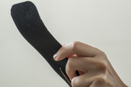 Physiotherapist cutting on black kinesio tape with a scissors.の写真素材