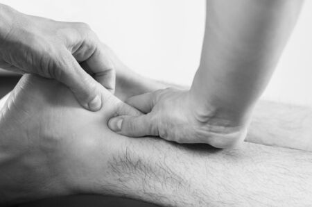 Closeup of hands of chiropractor/physiotherapist doing calf muscle massage to man patient in white and black.の写真素材
