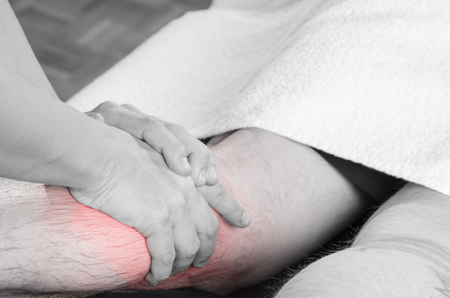 Closeup of hands of chiropractor/physiotherapist doing calf muscle massage to man patient,  in silhouette studio. Red color pain.の写真素材