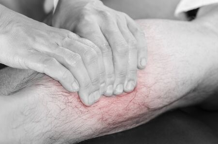 Closeup of hands of chiropractor/physiotherapist doing calf muscle massage to man patient,  in silhouette studio. Red color pain.の写真素材