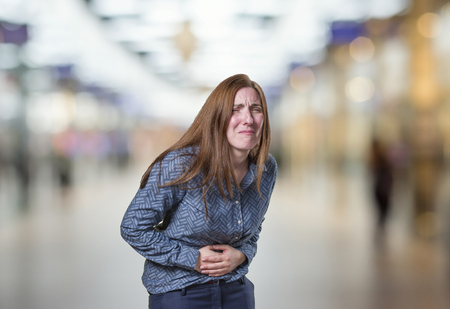 Pretty young happy business woman stomach pain over blur backgroundの写真素材