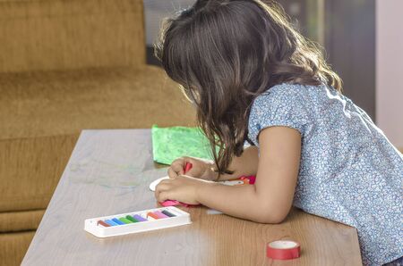 Cute little girl painting with crayon on a home interior background.
