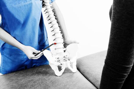 Doctor with a pen showing a hernia in a skeleton to a patient in silhouette isolated on white background.の写真素材