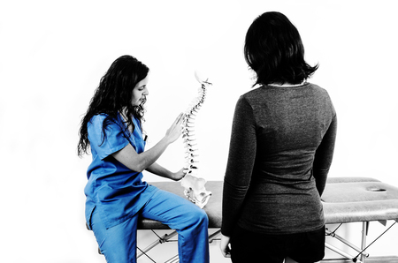 Doctor showing a skeleton to a patient. Back pain to a patient in silhouette isolated on white background.の写真素材