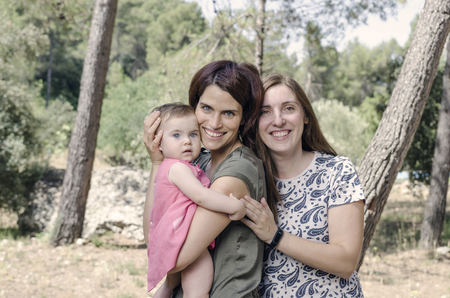 Portrait of happy lesbians mothers with a baby.  Homosexual family in a countrysideの写真素材