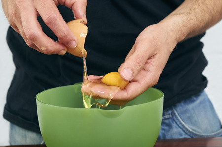 Close-up man's hands break the egg and separate the white from the yolkの写真素材