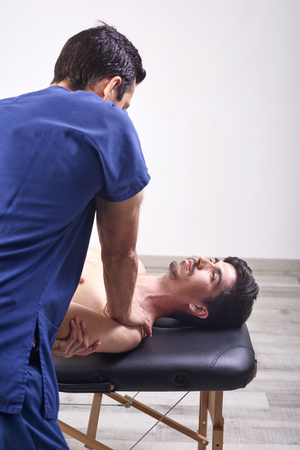 Young man having chiropractic shoulder adjustment. Physiotherapy, sports injury rehabilitation. Osteopathy, Alternative medicine, pain relief conceptの写真素材