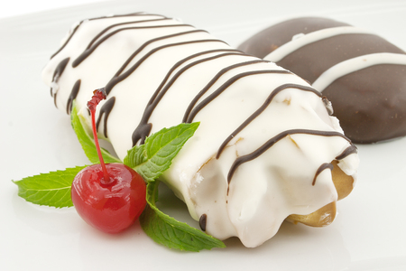 Eclair and biscuit with chocolate icing and mint, on white background. Selective focus