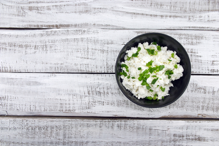 Cottage cheese with chives in black ceramic bowl on rustic wooden background. Healthy breakfast. Healthy food concept. Top view.の写真素材